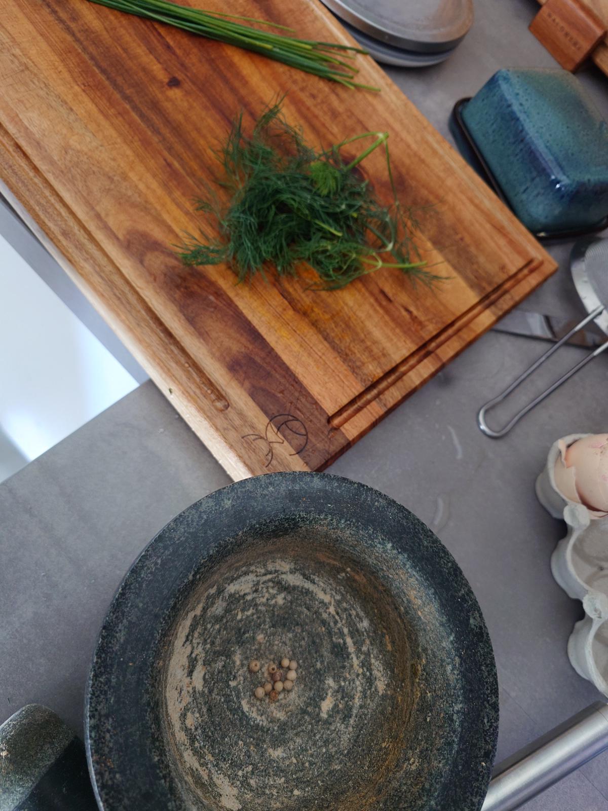 Dill and chives on the board, white peppercorns in the mortar