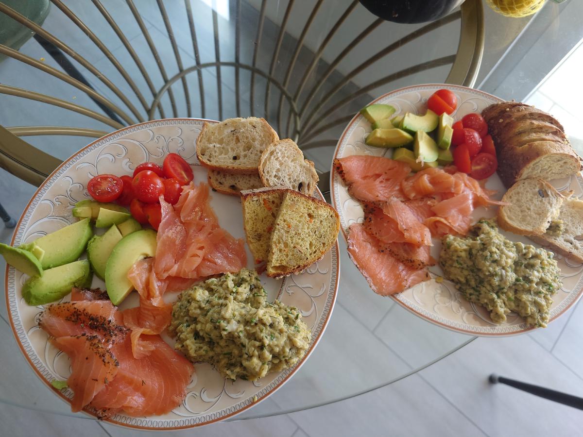 Two plates of scrambled eggs with smoked salmon, avocado, cherry tomatoes and bread