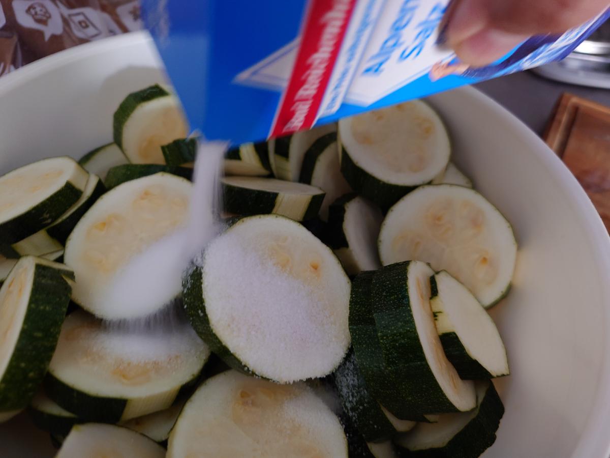 Salt poured from the box over sliced zucchini in a white bowl