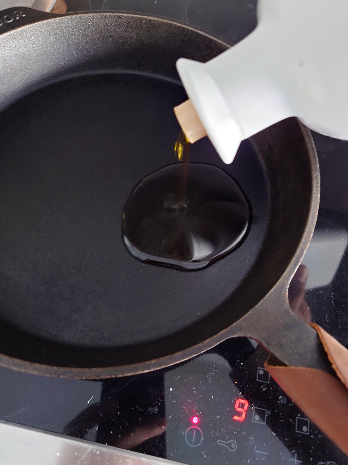 Oil poured from a white bottle into a cast iron pan, dial reading 9