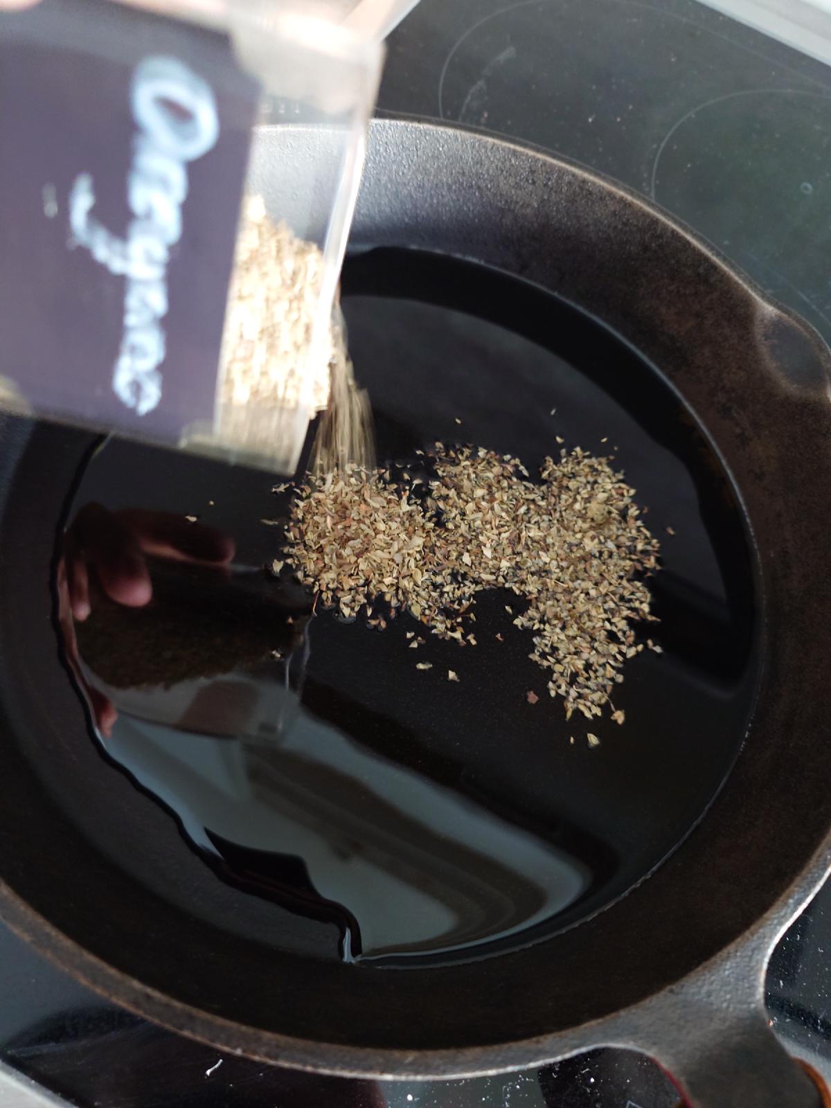 Dried oregano shaken from a bag into the hot oil