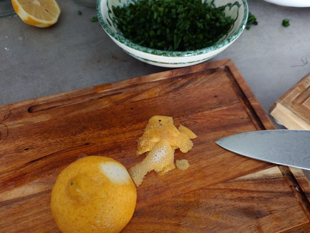 Zest peeled off the lemon on the board, chopped chives in a bowl behind